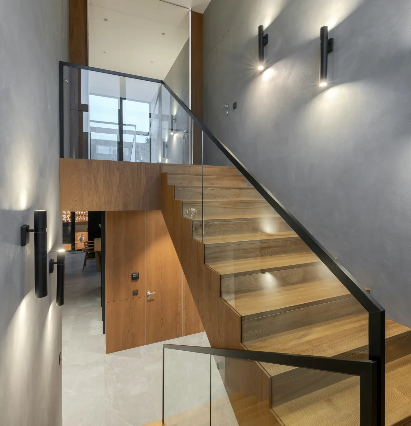 Escalier en bois le long d'un mur gris éclairé par des appliques murales